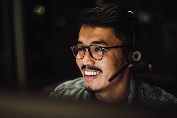 A smiling male customer service representatives uses a headset to talk to a customer via a call center service.